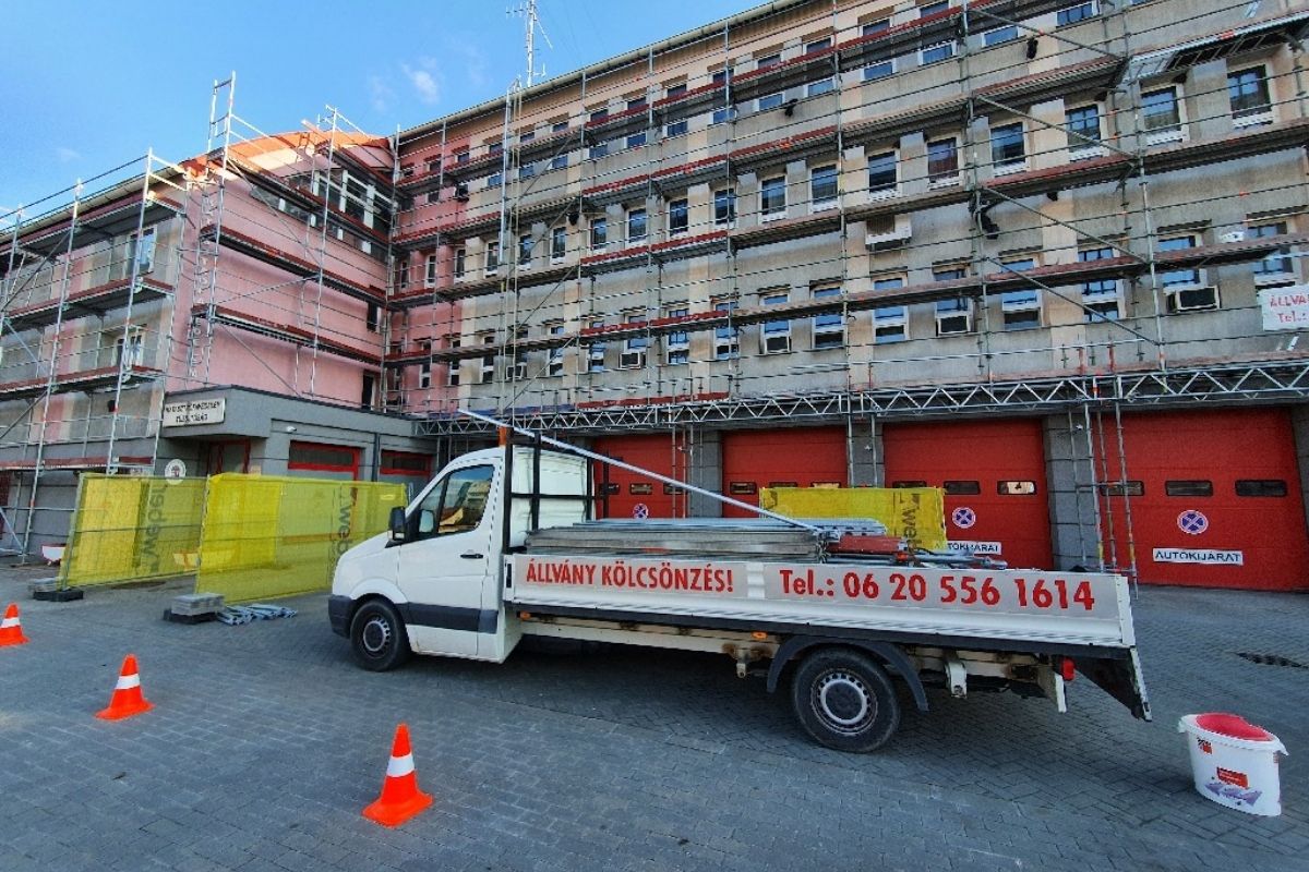 Ipari épület állványozása előtt parkoló teherautó állványelemek szállításával